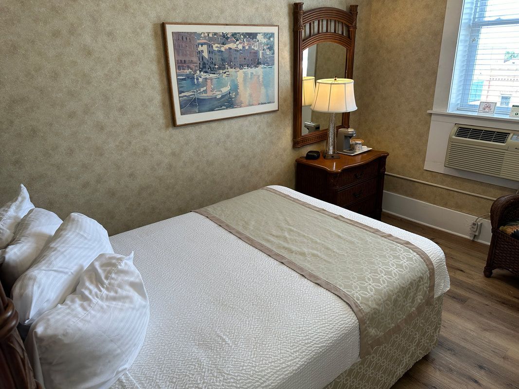 A hotel room with a bed , mirror , lamp and chair.