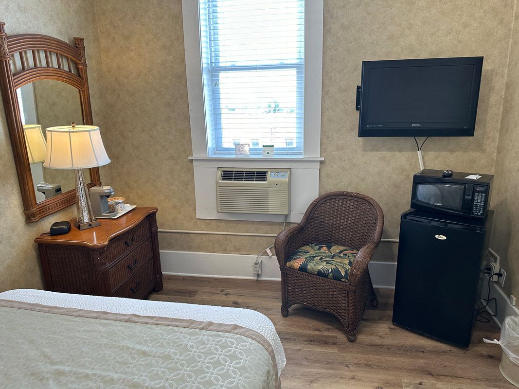 A hotel room with a bed , chair , dresser , microwave and television.
