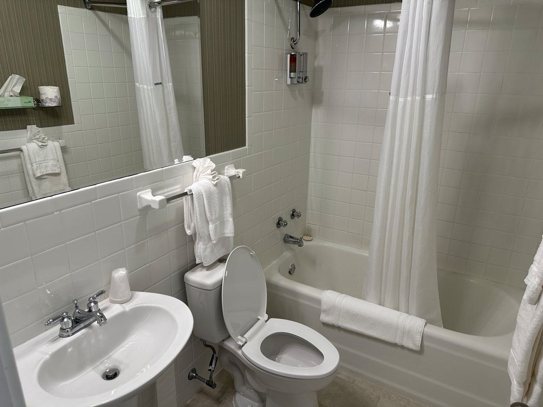 A bathroom with a toilet , sink , tub and mirror.