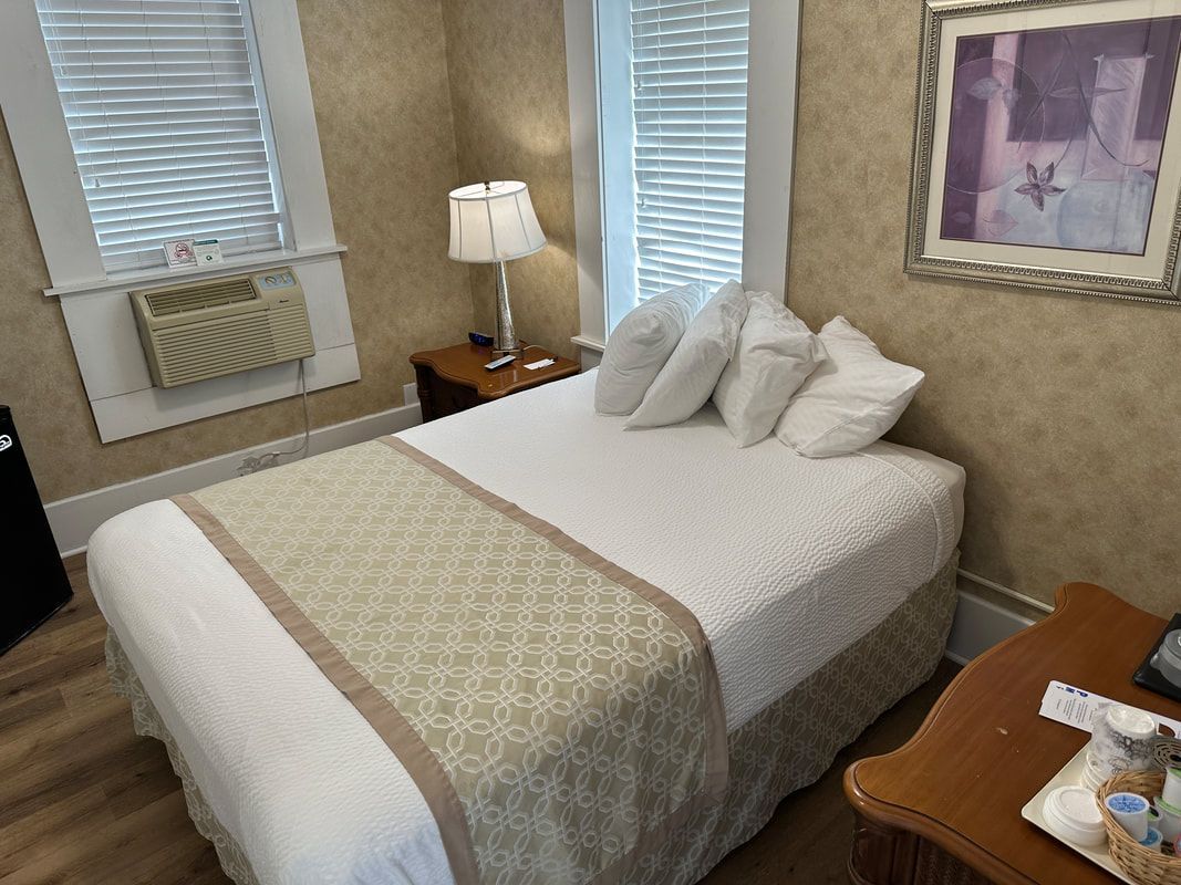 A hotel room with a bed , table , lamp and window.