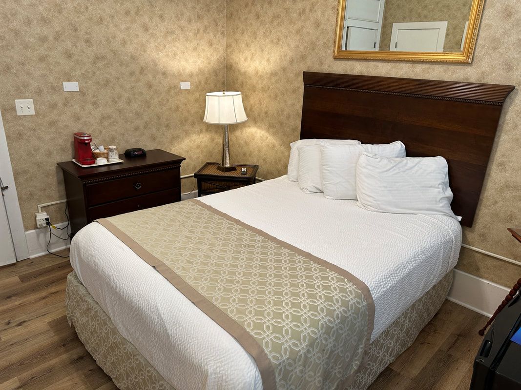 A hotel room with a bed , nightstand , lamp and mirror.