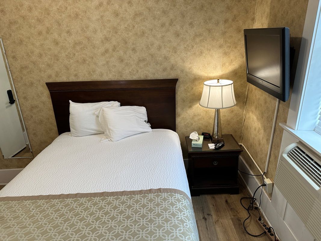A hotel room with a bed , nightstand , lamp and television.