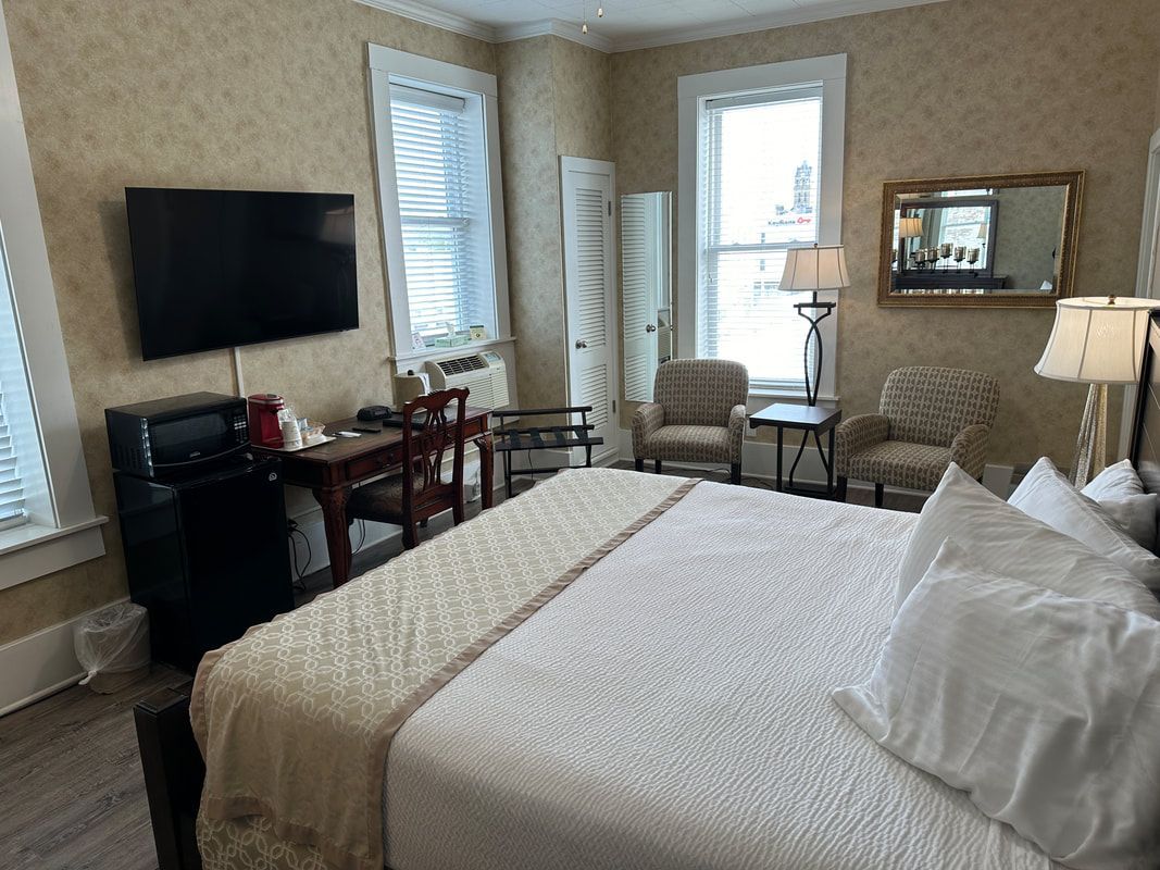 A hotel room with a king size bed , chairs , a desk and a flat screen tv.
