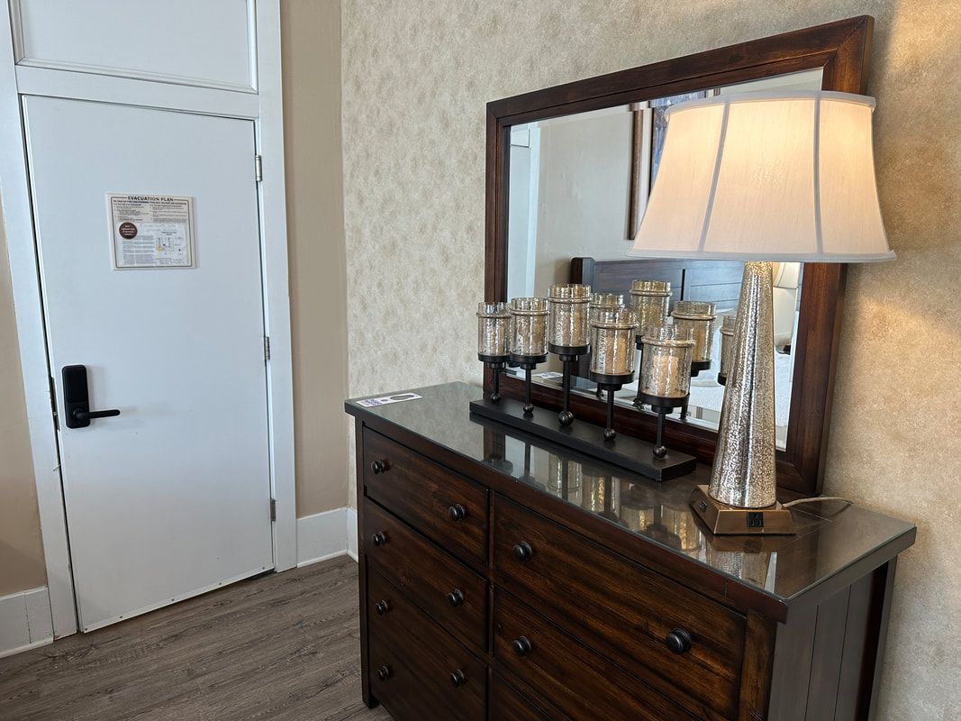 A bedroom with a dresser , mirror , lamp and candles.