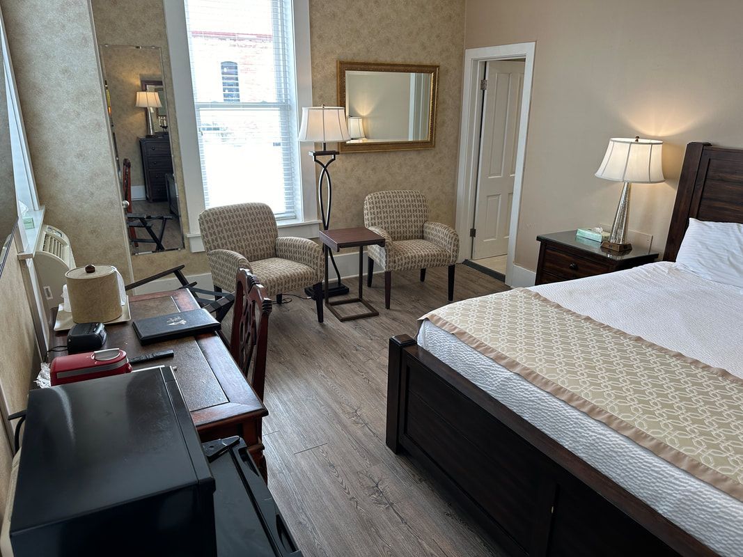 A bedroom with a bed , desk , chairs , lamps and a mirror.