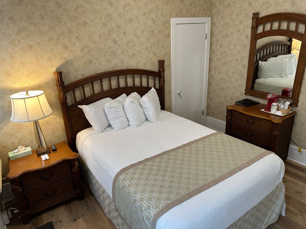 A bedroom with a bed , nightstand , lamp and mirror.