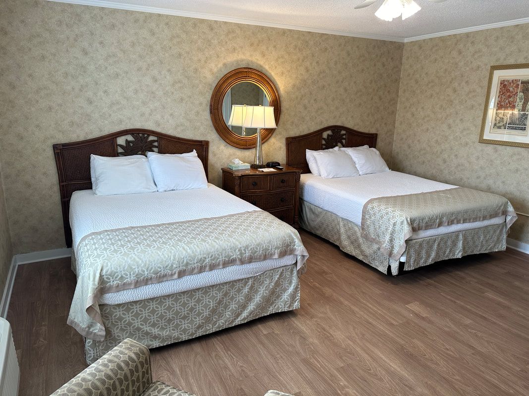 A hotel room with two beds , a chair and a mirror.