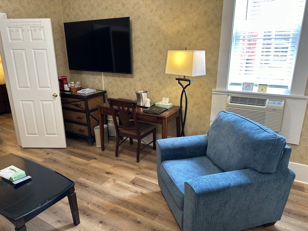 A living room with a blue chair , desk , television and coffee table.