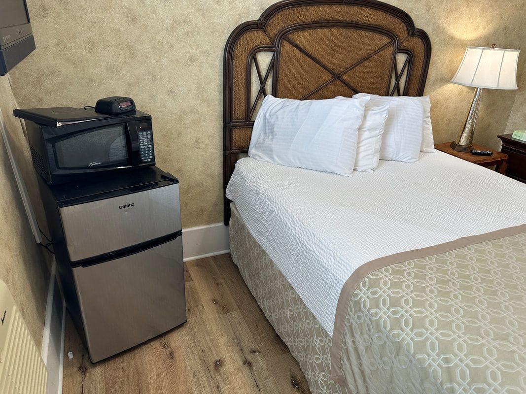 A hotel room with a bed , refrigerator , microwave and television.