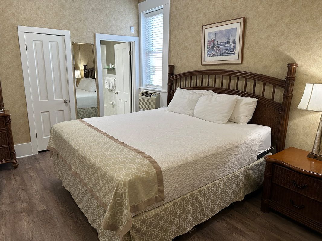 A bedroom with a king size bed , nightstand , lamp and mirror.