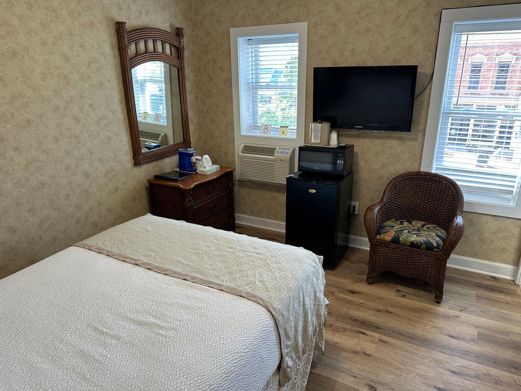 A bedroom with a bed , chair , television , refrigerator and microwave.