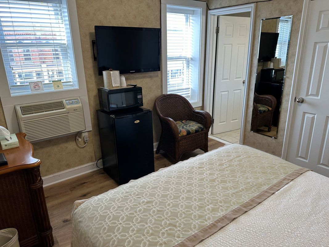 A hotel room with a bed , chair , refrigerator and television.