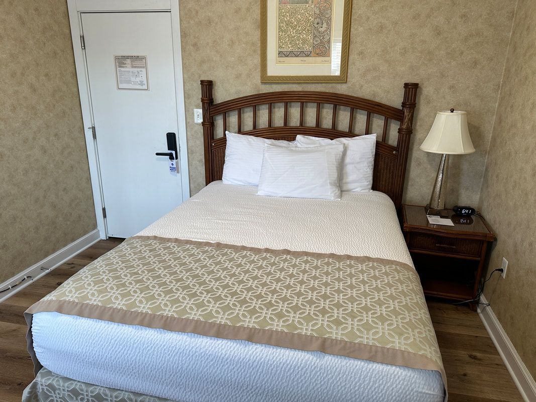 A hotel room with a bed , nightstand , lamp and door.