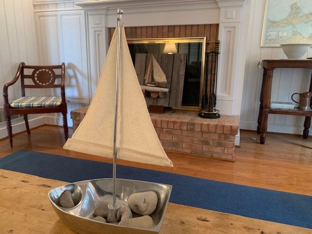 A small sailboat sits on a wooden table in front of a fireplace