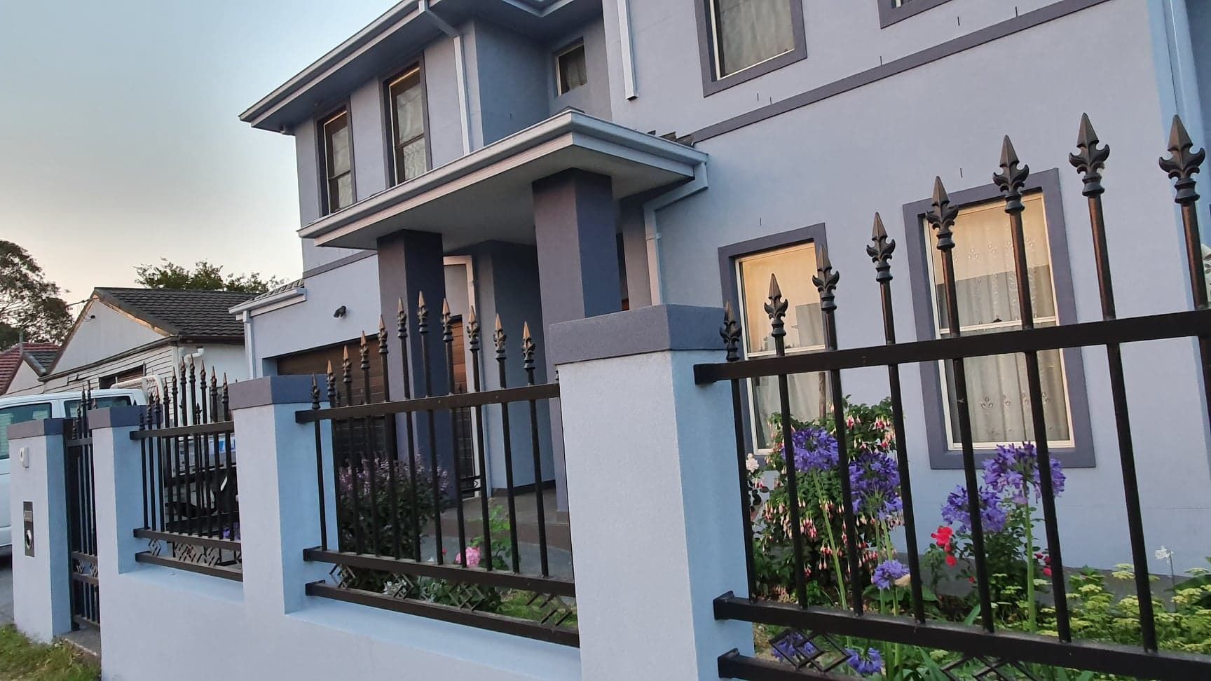 Modern two-story house with a black metal fence and a small front garden at dusk — Rendering By Yilmaz P/L In Shellharbour, NSW