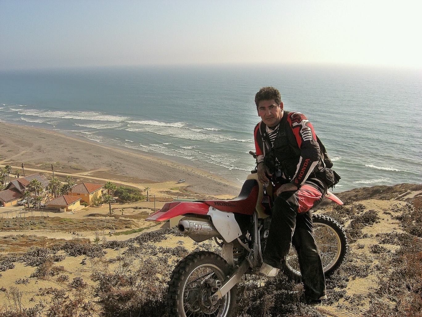 Person on a red dirt bike on a cliff overlooking the ocean