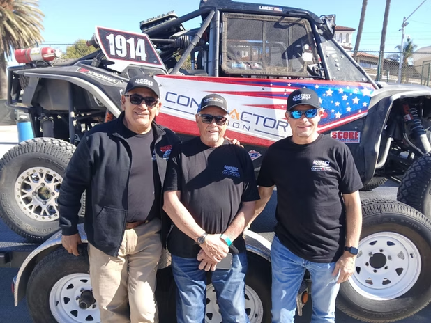 Three people posing in front of a race truck with a red, white, and blue star-spangled design