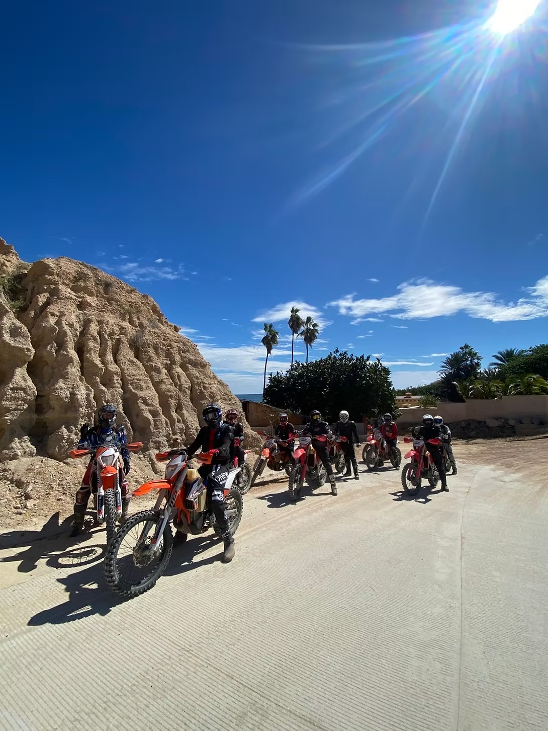 Cyclists racing on a sunny road beside rocky cliffs under a clear blue sky