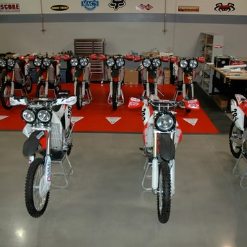 Rows of red dirt bikes in a showroom, with a white bike in the foreground.
