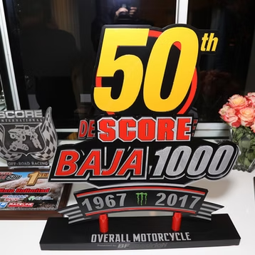 50th SCORE Baja 1000 commemorative plaque with red and yellow lettering, 1967–2017, on a black base
