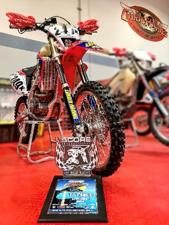 Decorated red dirt bike on display with a trophy plaque in front, at an indoor exhibit.