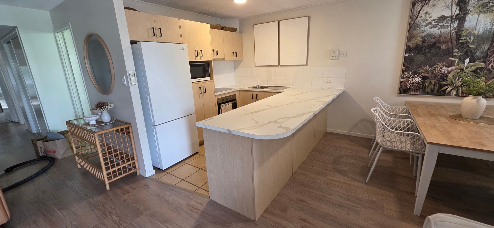 Bright kitchen and dining area with white cabinets, island, refrigerator, and wicker chairs by a wooden table — Suncoast Kitchens In Kunda Park, QLD