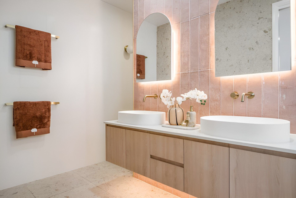 Modern bathroom with double sinks, light wood vanity, arched mirror, and copper wall accents— Suncoast Kitchens In Kunda Park, QLD