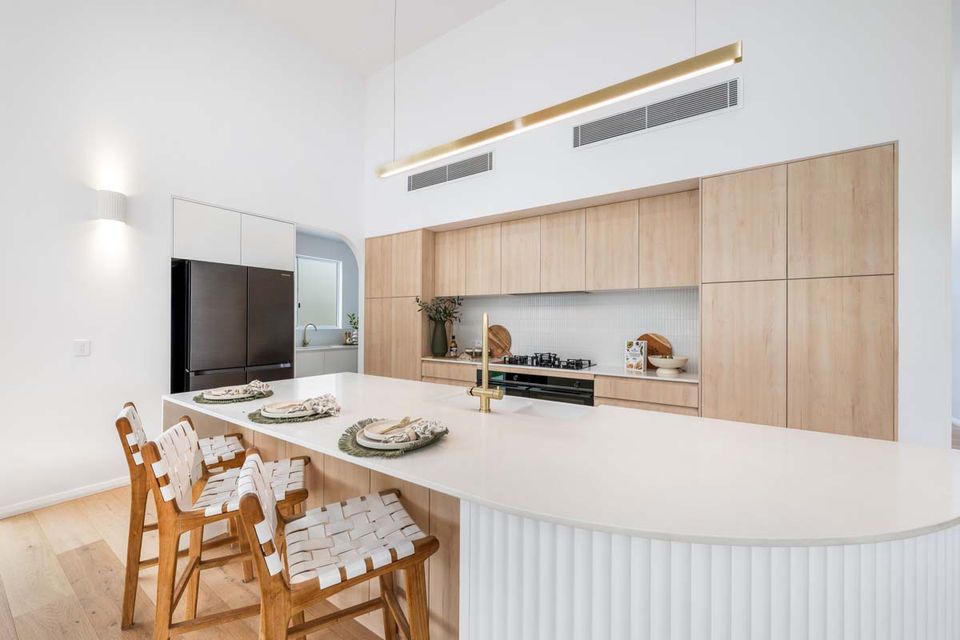 Modern white kitchen with curved island, wooden chairs, and light wood cabinets— Suncoast Kitchens In Kunda Park, QLD