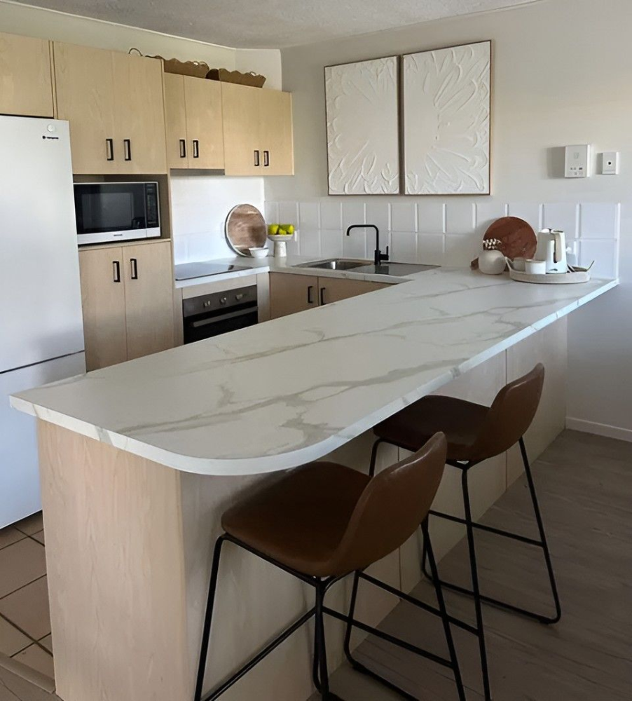 Modern kitchen with white island, light wood cabinets, stainless appliances, and two bar stools— Suncoast Kitchens In Kunda Park, QLD
