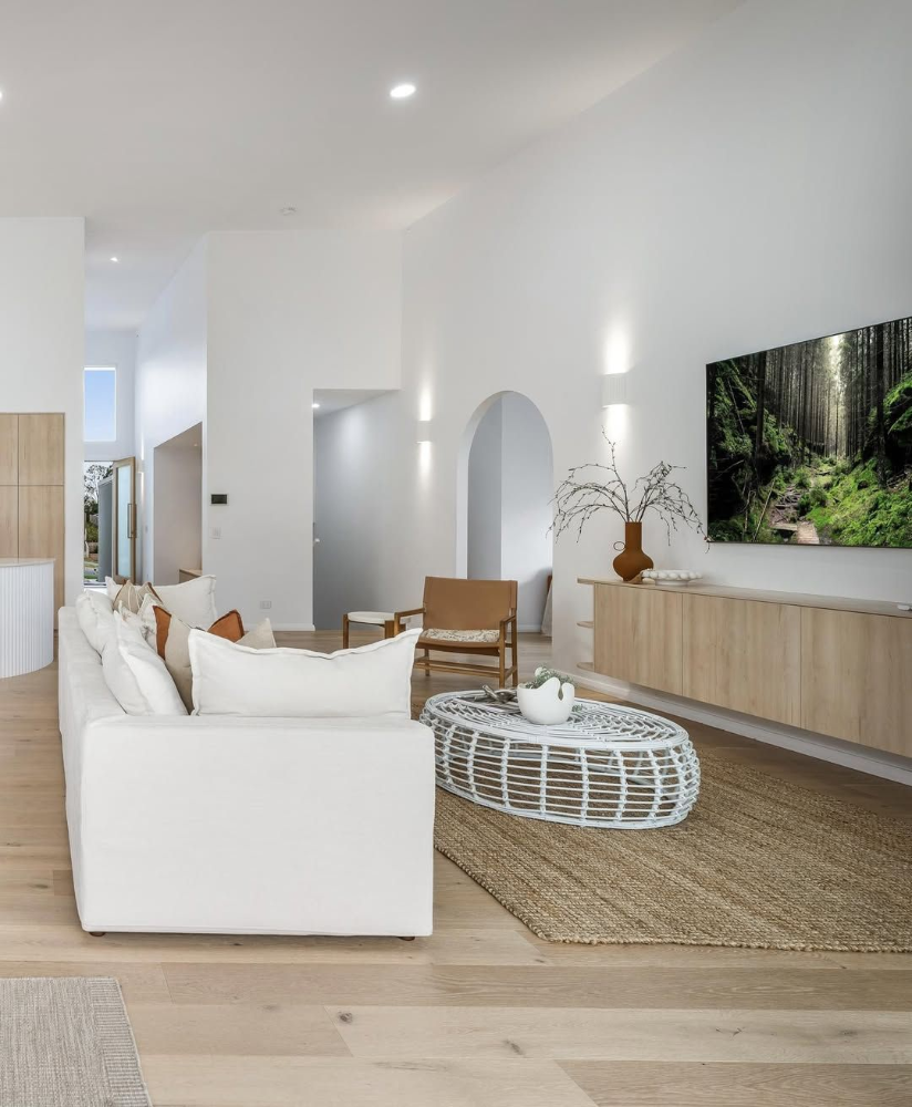 Modern white living room with sofa, woven coffee table, wood console, and TV showing a forest scene— Suncoast Kitchens In Kunda Park, QLD
