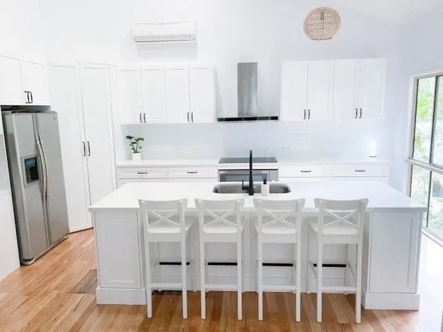 A Kitchen With White Cabinets, Stools, a Refrigerator and a Sink — Suncoast Kitchens In Kunda Park, QLD