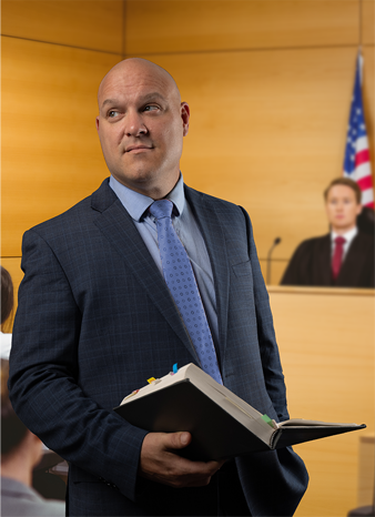 A man in a suit and tie is holding a book in a courtroom.