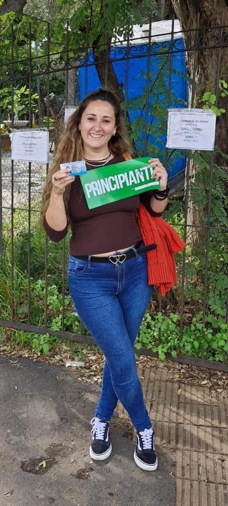 Mujer sosteniendo un cartel verde, de pie al aire libre junto a una valla y unos árboles.