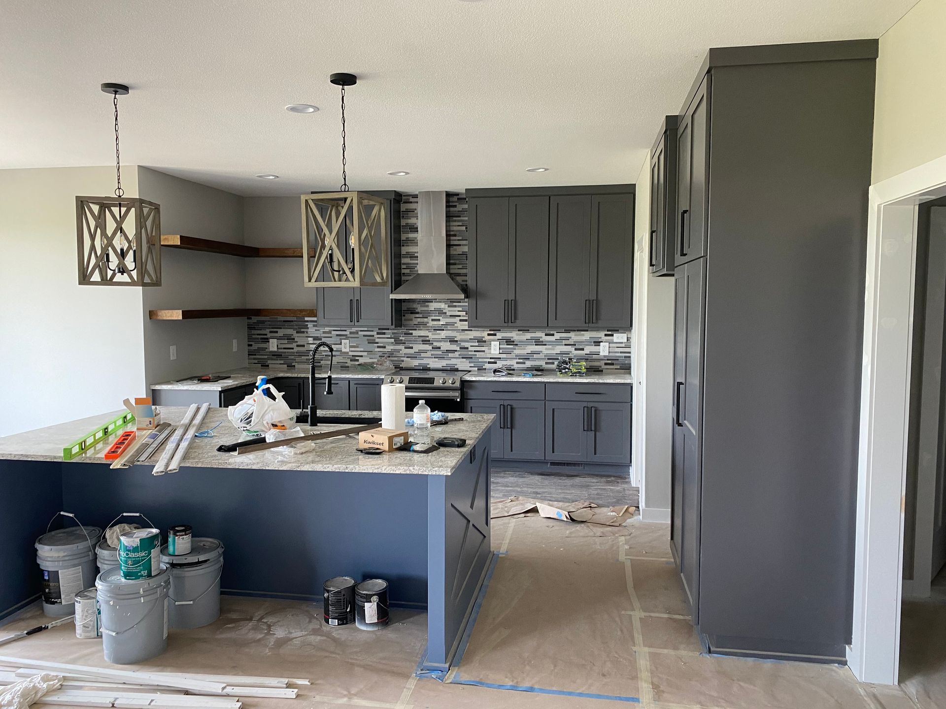 Modern kitchen under renovation with gray cabinets, central island, and construction materials on the floor