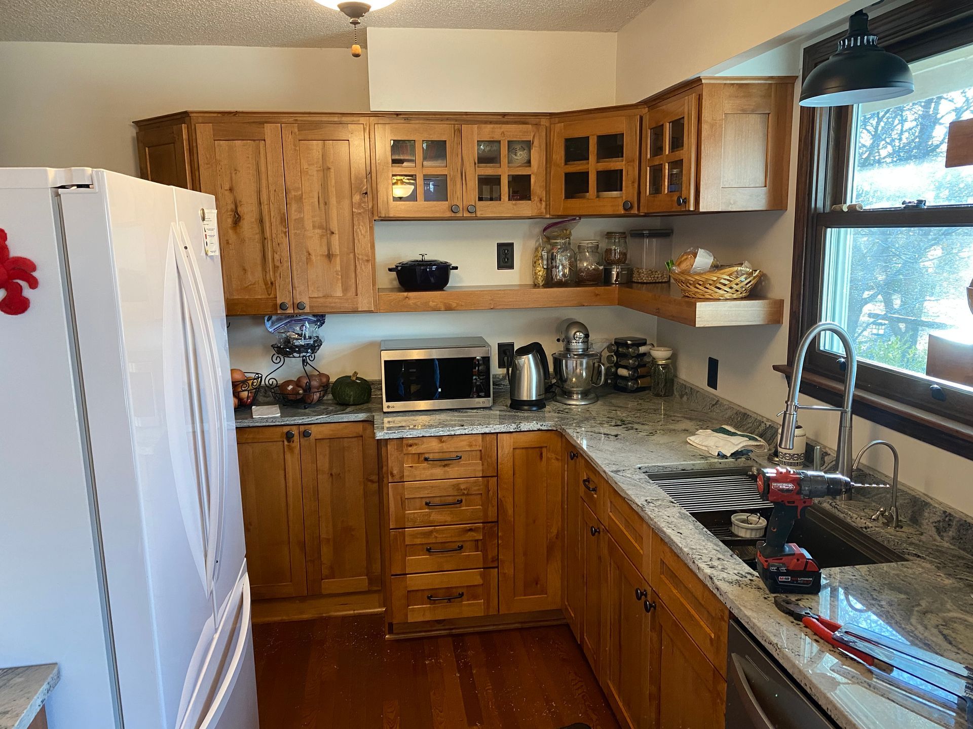 Small kitchen with white fridge, wooden cabinets, beige counters, and a window over the sink.