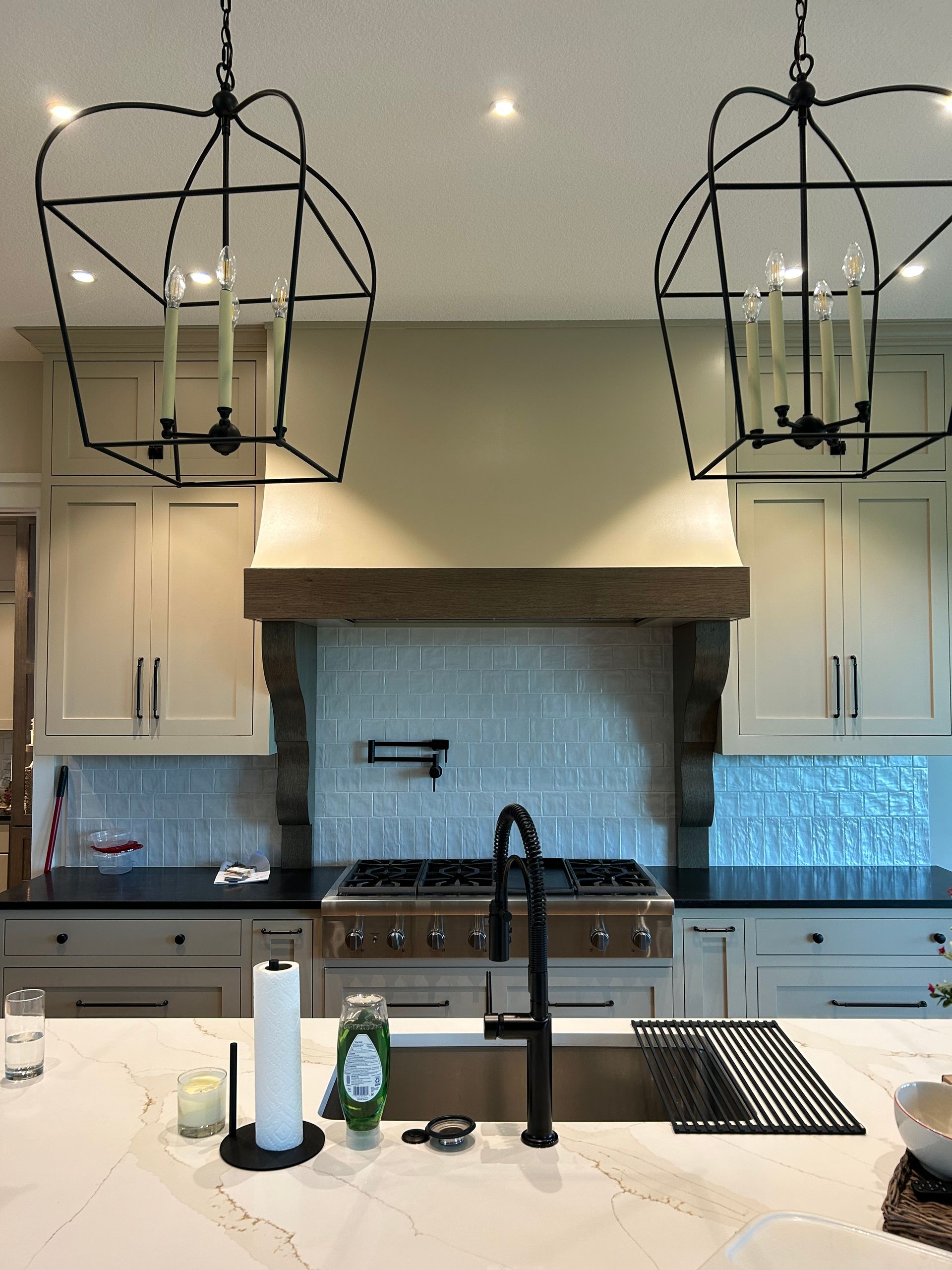 Bright kitchen with white cabinets, black range hood, blue tile backsplash, and island with black faucet and pendant lights