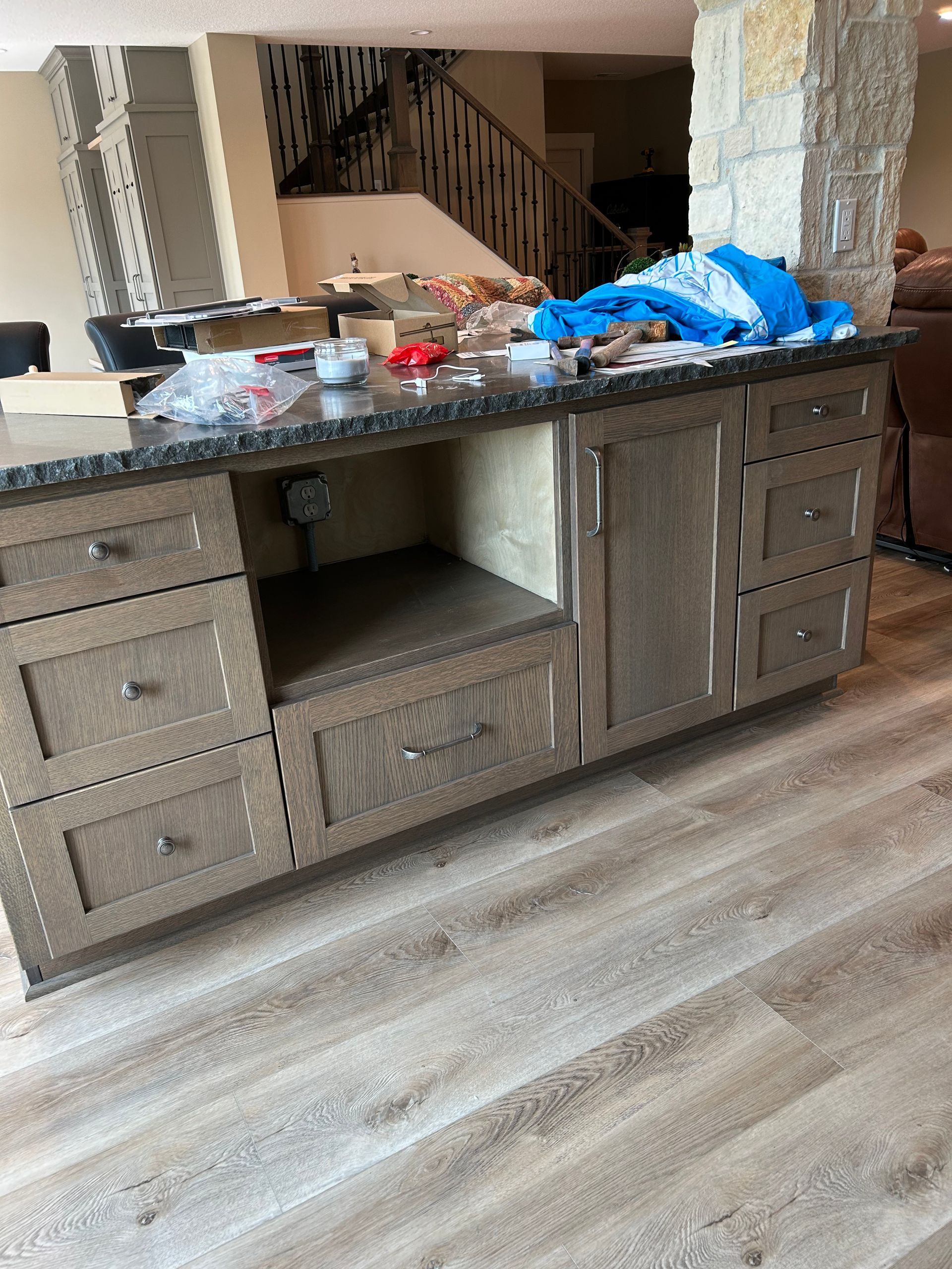Kitchen island cluttered with items, dark cabinets, and a light wood floor in an open room.