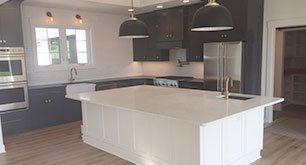 Modern kitchen with a large white island, black pendant lights, dark cabinets, and stainless steel appliances.