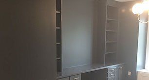 Built-in gray cabinets and shelving in a home office or media room with a window on the right.