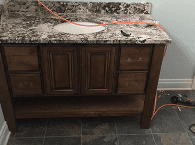 Dark wood bathroom vanity with marble countertop, sink cutout, and orange extension cord on top.