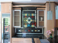 Modern kitchen with a colorful tiled backsplash, black countertop, and light wood cabinets.