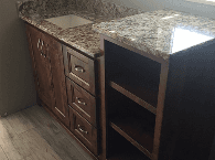 Granite kitchen countertop with double sink, wooden cabinets, and open shelving under construction