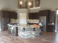 Modern kitchen with stone island, dark cabinets, wood floors, and pendant lights