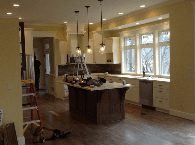 Modern kitchen with island, pendant lights, hardwood floors, and large windows overlooking a yard