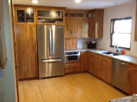 Empty modern kitchen with wood cabinets, stainless steel fridge, and bright window over the sink