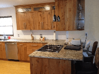 Modern kitchen with wooden cabinets, granite island, stove, sink, and dining chairs by a window
