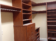 Walk-in closet with wooden shelves, hanging rods, and dresser drawers in a beige room