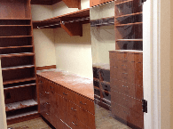 Walk-in closet with wooden shelves, drawers, and hanging rod, seen through an open doorway