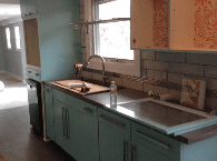 Kitchen counter with sink, faucet, teal cabinets, and light wood upper cabinets by a window.