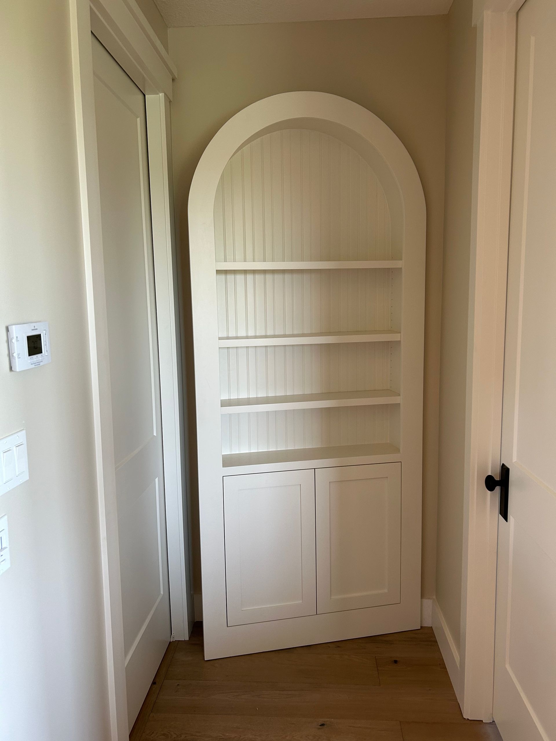White arched built-in bookshelf in a narrow hallway with wooden floor and beige walls